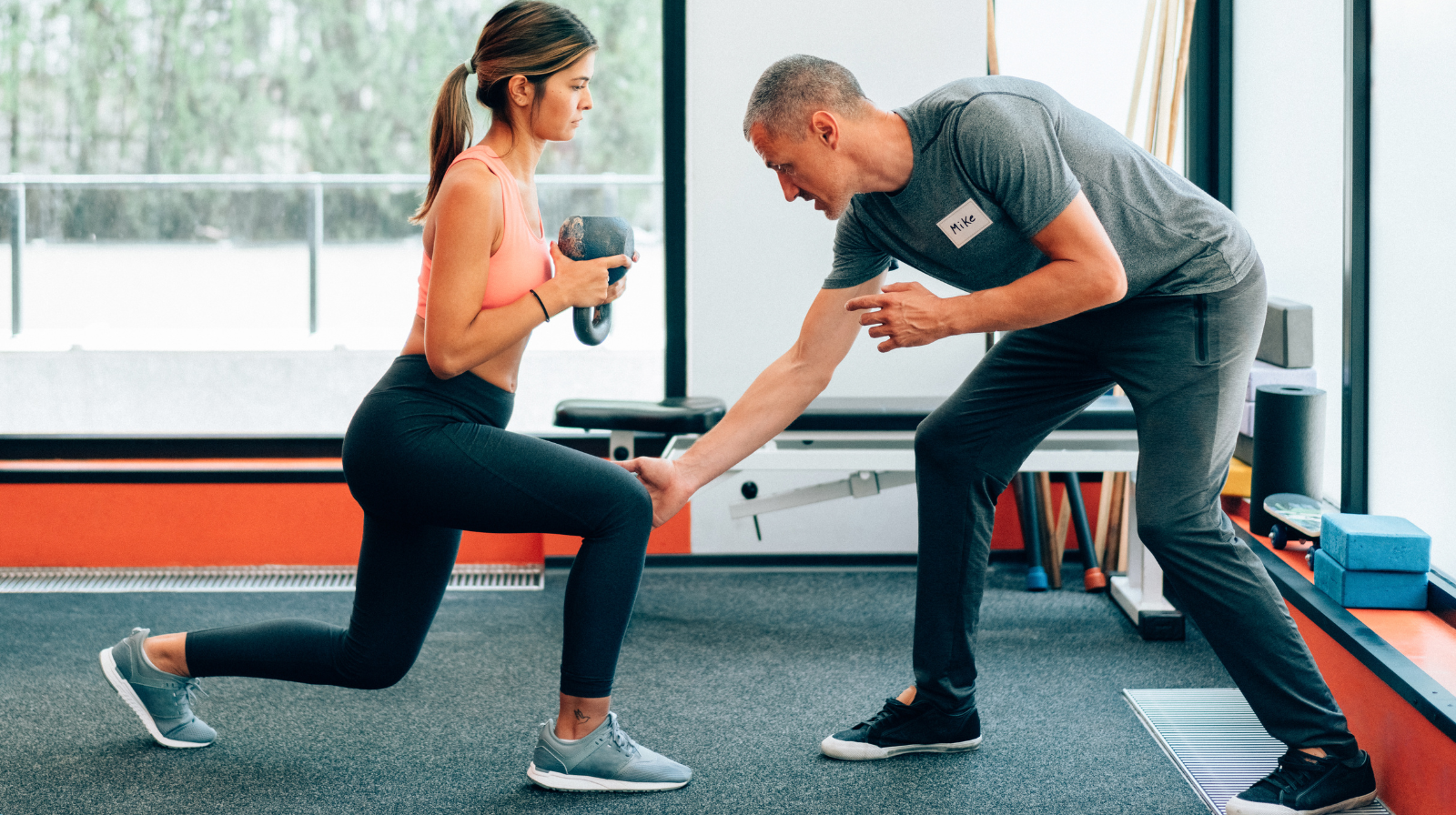 Personal trainer coaching a client through a kettlebell lunge in a gym